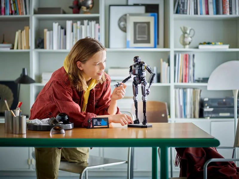 Child playing with a robot toy at a table in a room with bookshelves.